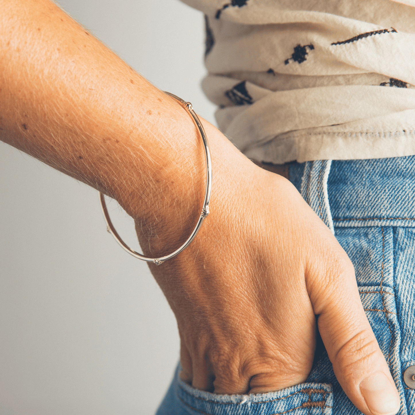 The sunflower bangle hangs on a woman's wrist as she tucks hands into pockets