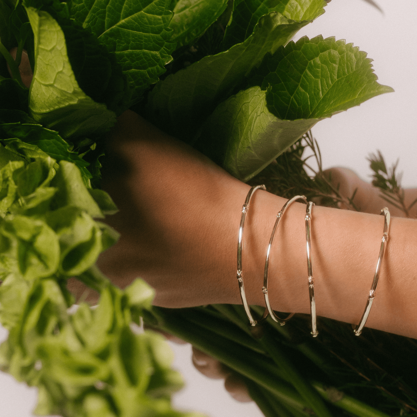 The sunflower bangle stacked with other golden bangles on a woman's wrist as she holds flowers
